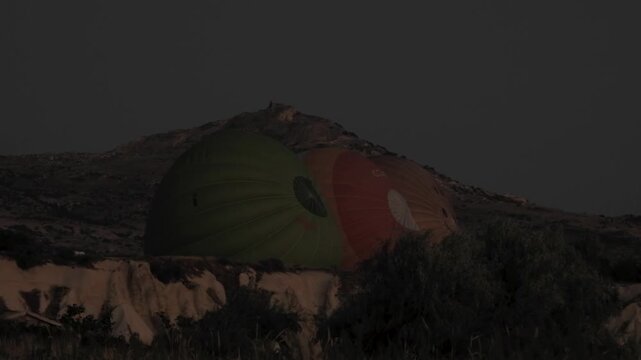 Hot air balloon inflation preparations begin at a dark launch site before sunrise.