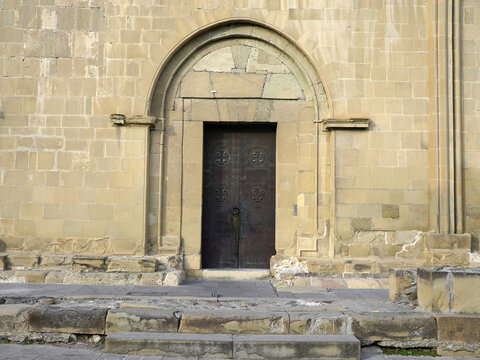 An arched stone portal with an ornate dark wooden entrance door is set into the carved sandstone facade of Svetitskhoveli Cathedral in Mtskheta, Georgia