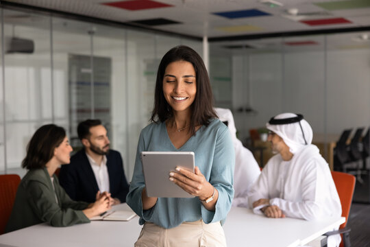 Smiling Latina businesswoman stands in office, working on project using digital tablet, reviewing information, managing corporate tasks, checking report. Application, modern technology use in business