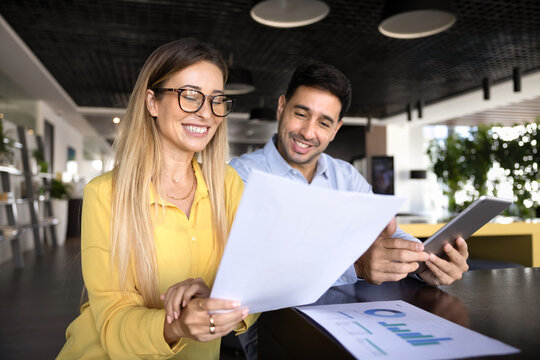 Colleagues sitting together in modern office, reviewing printed documents and discussing data charts, working on performance metrics, reports, or business strategy, smiling, feel satisfied with result