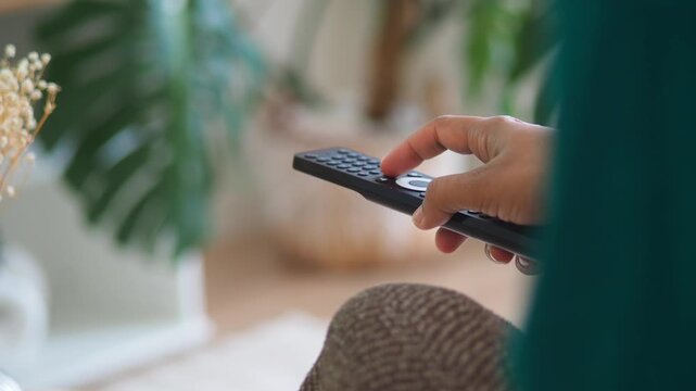 Person's hand using remote control to change channel on television close up slow motion.