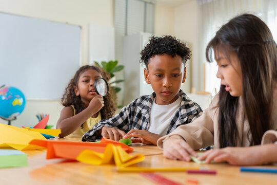 Diverse school children folding paper in kindergarten class, Multiethnic kids doing origami paper craft in classroom, Cute african american boy and asian girl learning arts and crafts at school desk