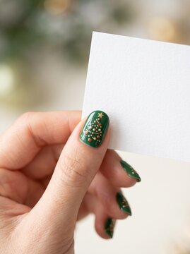 Woman hand with festive green Christmas tree nail art holding a blank white card for holiday greeting mockup.