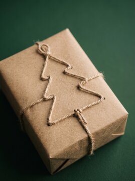 Rustic eco-friendly gift box wrapped in brown kraft paper with twine tied in a Christmas tree shape on green background.