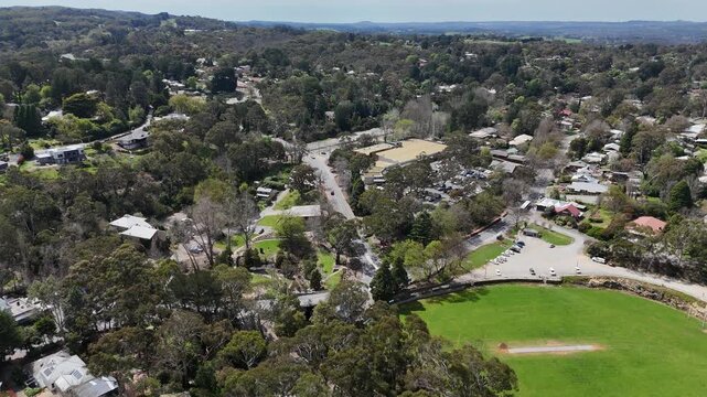 Aerial drone view over the town centre of Bridgewater in the Adelaide Hills, South Australia, Australia, with traffic flow on the main street, shopping precinct and car park, a large green sports oval