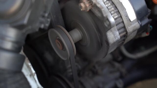 Close-up of a running car engine showing alternator pulley and drive belt spinning with motion blur, capturing mechanical power, maintenance concept, and engineering. 4K video.