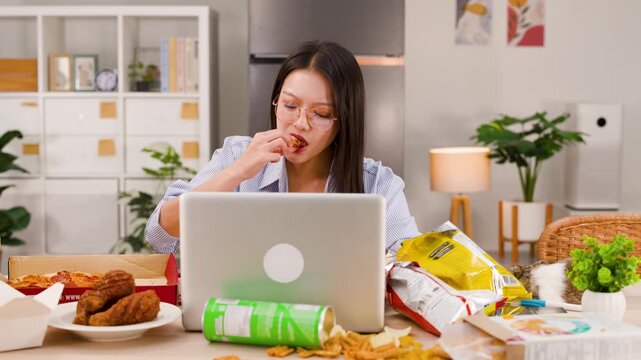 Asian Woman Eating Fried Chicken While Working on Laptop at Home