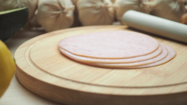 Fresh slices of circular ham on wooden cutting board with garlic and knife in kitchen scene.