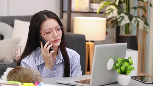 Stressed Asian Woman Talking on Smartphone While Working from Home