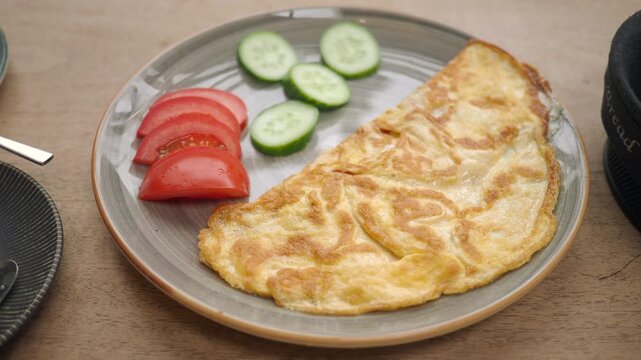Close-up motion of folded omelette with sliced tomatoes and cucumber on plate.