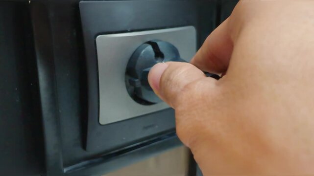 Close Up of Hand plugging a blck power plug into an electrical wall socket to charge a device.