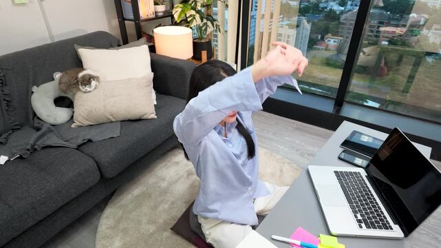 Asian Freelancer Stretching While Working on Laptop in Modern Apartment