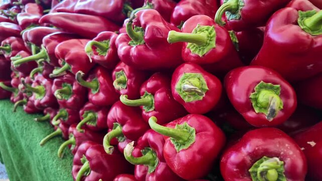 Fresh red bell peppers displayed on a green cloth at a local outdoor market stall.
