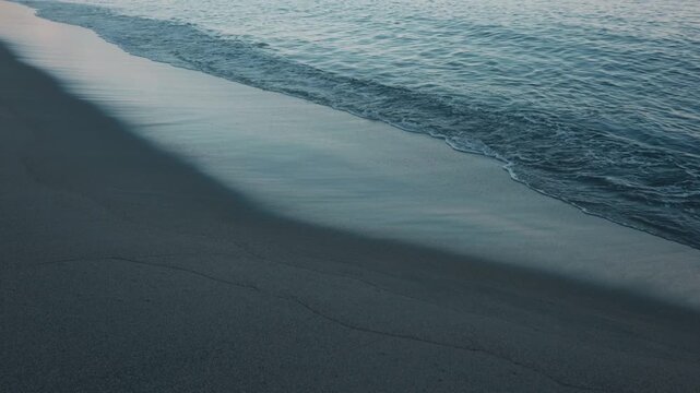 Gentle waves quietly lapping against a smooth, light gray sandy beach