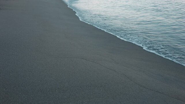 Gentle waves quietly lapping against a smooth, light gray sandy beach
