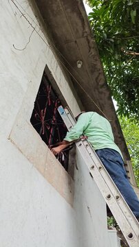 Young Man On Ladder Painting High Window Frame Exterior
