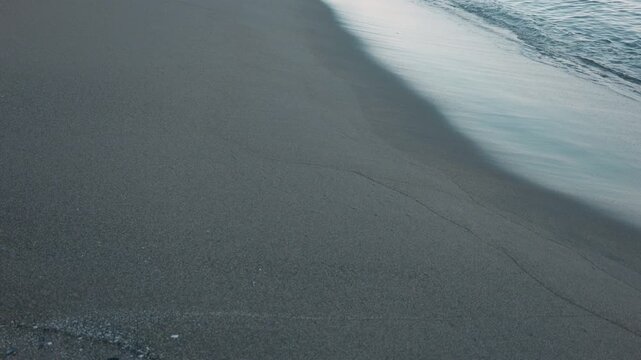 Gentle waves quietly lapping against a smooth, light gray sandy beach
