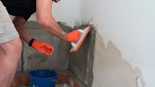 Worker plastering a rough concrete wall with a float
