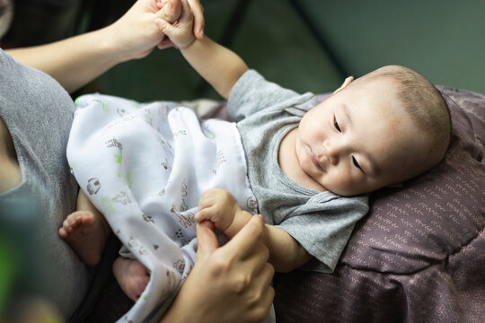 Motherhood tender bonding and newborn care concept, mother gentle hands holding infant hands and feet on pillow under soft blanket, representing maternal love, pediatric health, and soothing.