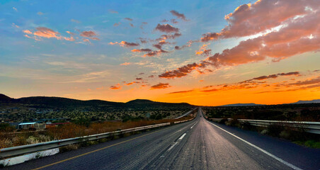 Desert Highway at Sunset: An endless highway stretches into the horizon, silhouetted against a dramatic sunset sky painted with vibrant oranges, pinks, and purples. © Jerrysv