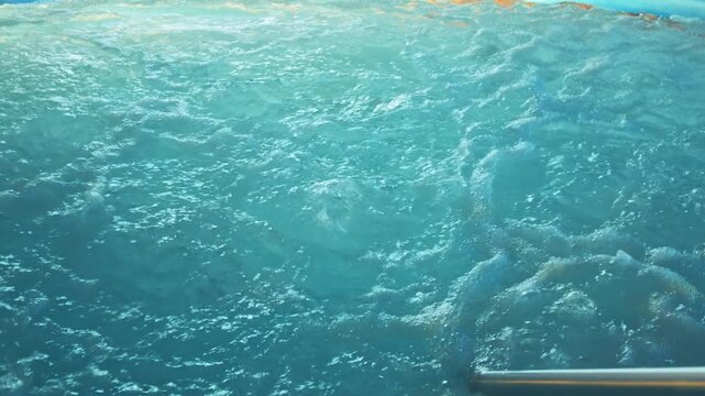 Churning, swirling turquoise water inside a luxury jacuzzi hot tub whirlpool with stainless steel safety handrails in the foreground