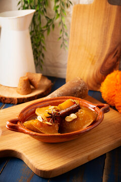 Vertical shot of Mexican sweet candied pumpkin dessert, calabaza en tacha, garnished with cinnamon and star anise in a clay plate on wooden cutting board with piloncillo background.