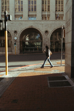 Woman with coffee walks across a sunny city street