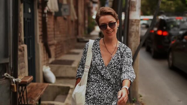 Happy stylish woman in a dress walks down a city street