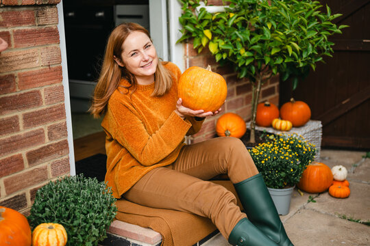 A smiling woman holding a pumpkin outside, autumn scene