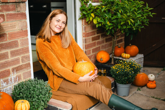 Happy woman sitting on doorstep with autumn pumpkin decorations