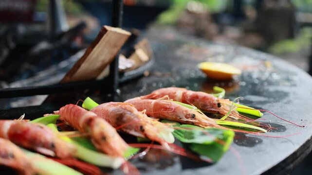 Fresh prawns with green onion cooking on hot black grill plate. Seafood barbecue preparation outdoors. Grilled shrimp with leek stems, healthy food and street food concept.