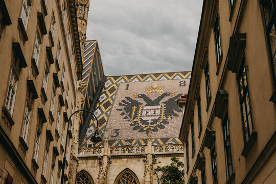 close upward view of ornate church roof tiles with double headed eagle crest between historic buildings