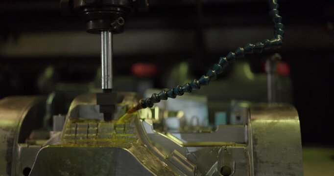 Milling machine cutting a large steel mould with cutting fluid flowing in a machining shop
