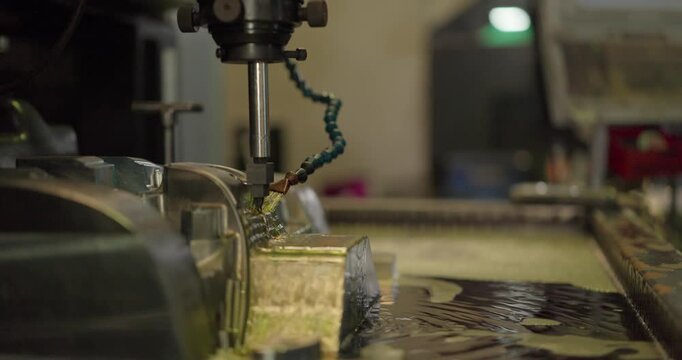 Milling machine cutting a large steel mould with cutting fluid flowing in a machining shop