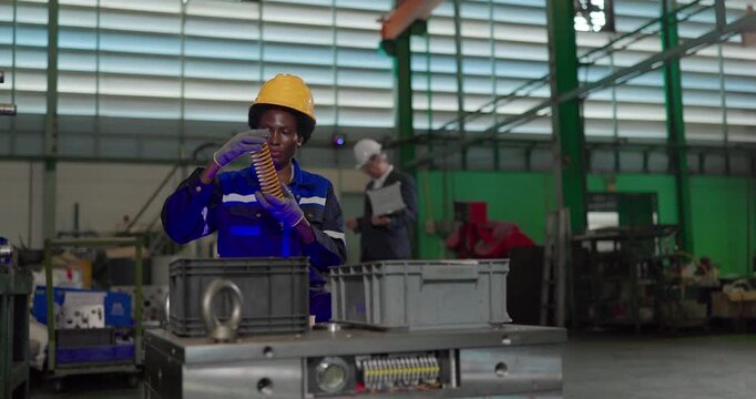 African woman technician inspecting a yellow coil die spring beside a large steel mould