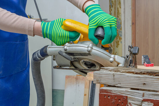 Gloved hands operating a circular saw to cut reclaimed lumber at an angle in workshop. Carpentry and woodworking project. Power tool safety and protective equipment. DIY renovation and material reuse