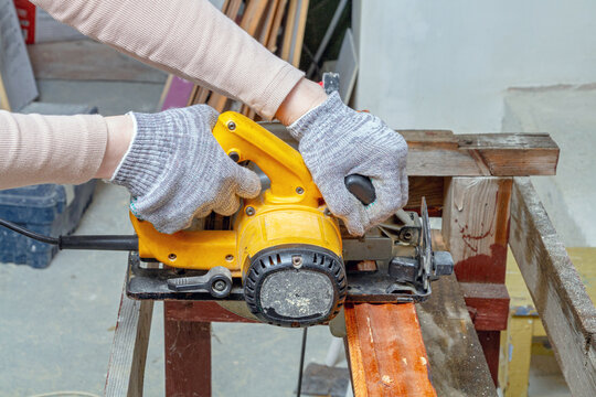 Gloved hands guiding a circular saw through timber in a workshop, top view. Woodworking and carpentry. Power tool operation and DIY renovation. Construction, repair and home improvement