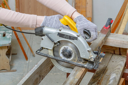 Hands of a worker operating a circular saw to cut lumber in a workshop. Power tool woodworking and carpentry. Construction and home renovation project. DIY building and timber cutting