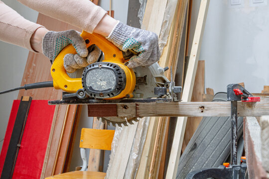 Gloved hands guide a circular saw through lumber in a workshop. Woodworking and carpentry. DIY renovation and home improvement. Power tool safety and construction work projects