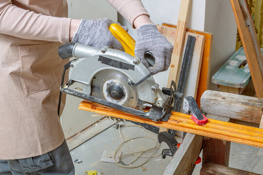 Person cutting a wooden plank with a handheld circular saw in a workshop. Carpentry and woodworking. DIY home repair and renovation projects. Construction and woodworking craft