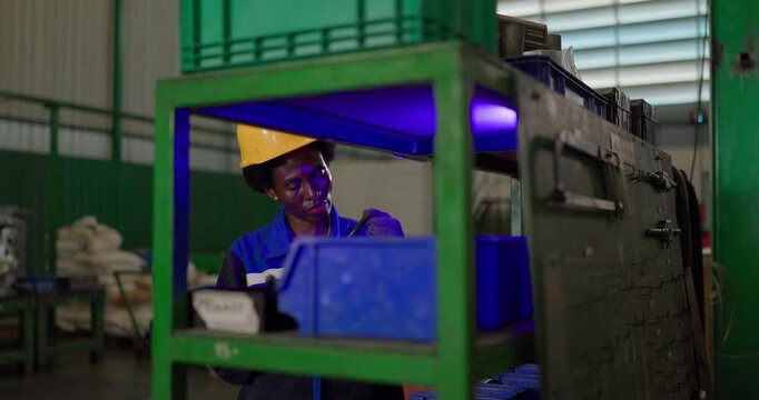 African woman technician checking ejector pins at a tooling storage rack in a factory tool crib