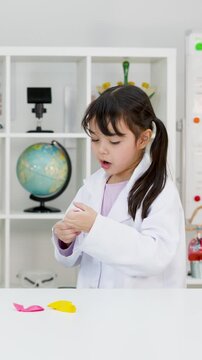 Little Asian Girl in Lab Coat Blowing Up Balloon in Science Classroom