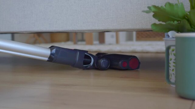 Low profile vacuum cleaner head cleaning hardwood floor surface under couch in living room.