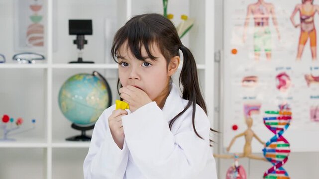 Young Schoolgirl in Lab Coat Blowing Up Balloon in Science Classroom