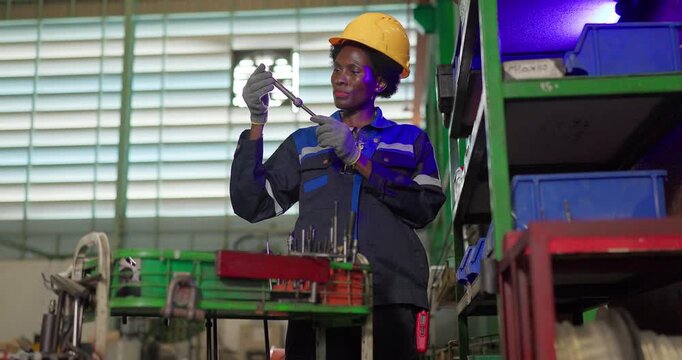 African woman technician checking ejector pins at a tooling storage rack in a factory tool crib