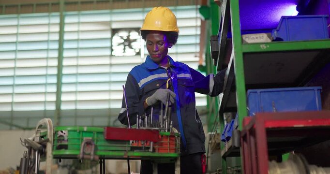 African woman technician checking ejector pins at a tooling storage rack in a factory tool crib