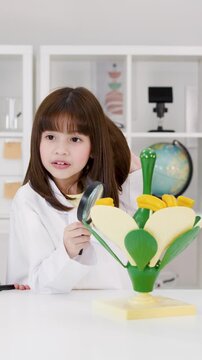Young Girl in Lab Coat Examining Flower Model with Magnifying Glass
