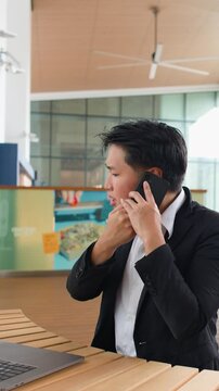 Stressed Asian Businessman Talking on Smartphone at Outdoor Cafe