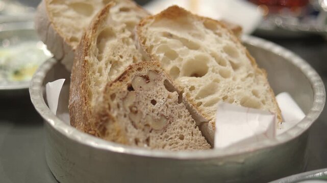 Close up of hand taking yellow bread slice from metal bowl of assorted bread slices.