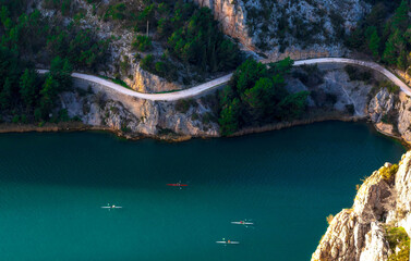 High angle view of rowers in kayaks on green river surrounded by cliffs and winding road © Sonja